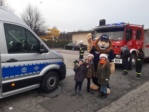 zaparkowany radiowóz obok 3 dzieci w towarzystwie Komisarza Lwa- maskotki dolnośląskiej policji