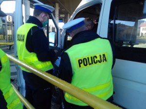 kontrola środków transportu pod katem przestrzegania przepisów dotyczących COVID 19, dwóch umundurowanych policjantów kontroluje bus przewożący osoby