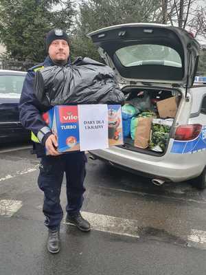 policjant niesie zebrane rzeczy dla osób z Ukrainy