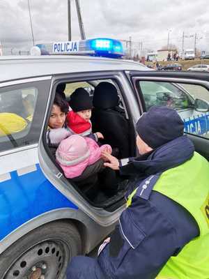 matka z dziećmi siedzi w radiowozie, obok jest policjant w mundurze