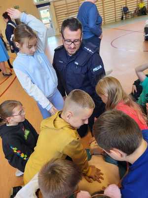 policjant z dziećmi ćwiczy jak reanimować. Widać policjanta i dzieci wokół manekina leżącego na macie