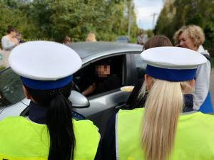 policjantki stoją tyłem, brunetka i blondynka a na drugim tle dzieci obok auta