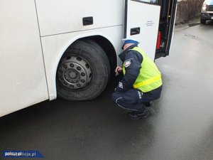 na zdjęciu część przednia autobusu a z boku policjant który sprawdza opony